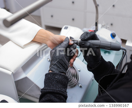 Manicurist removes nail polish uses the electric machine of the nail file during manicure Manicurist removes nail polish uses the electric machine of the nail file during manicure 138990167