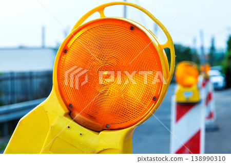 Closeup of a range warning beacon mounted on a red and white roadwork barrier on quiet street. Construction safety and traffic control 138990310