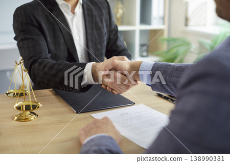 Male lawyer shaking hand with a man client sitting at the desk on workplace in office. Male lawyer shaking hand with a man client sitting at the desk on workplace in office. 138990381