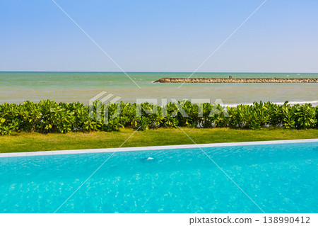 Tranquil ocean view with an infinity pool and lush green hedge Tranquil ocean view with an infinity pool and lush green hedge 138990412