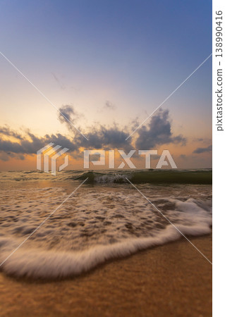 Gentle ocean waves lap onto a sandy beach at sunset with colorful clouds 138990416