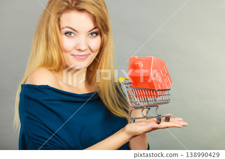 Woman holding shopping cart with house inside Woman holding shopping cart with house inside 138990429