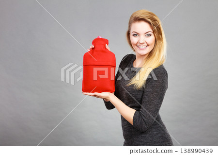 Happy woman holds hot water bottle Happy woman holds hot water bottle 138990439