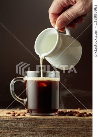 Coffee in a clear glass mug with cream being poured. 138990962