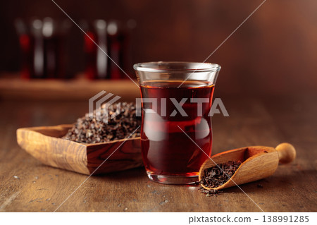 Glass transparent cup of black tea and dry tea in old wooden dish. Glass transparent cup of black tea and dry tea in old wooden dish. 138991285