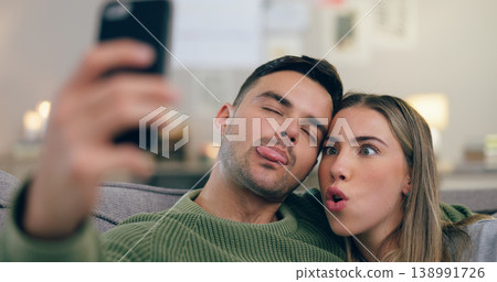 Couple, sofa and selfie with funny face in home living room with cross eyes, tongue and together for web blog. Man, woman and comic memory with photography for profile picture on social network app Couple, sofa and selfie with funny face in home living room with cross eyes, tongue and together for web blog. Man, woman and comic memory with photography for profile picture on social network app 138991726