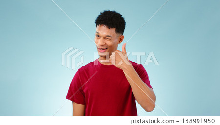 Portrait, man and wink to call me in studio on blue background in communication mockup. Cape Town, male model and flirting with hand emoji for connection, cellular or network with contact in space Portrait, man and wink to call me in studio on blue background in communication mockup. Cape Town, male model and flirting with hand emoji for connection, cellular or network with contact in space 138991950