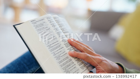 Hand, bible study and closeup for reading in home for faith, knowledge or spiritual information on sofa. Person, zoom and book for hope, worship or connection to God in living room for peace in house Hand, bible study and closeup for reading in home for faith, knowledge or spiritual information on sofa. Person, zoom and book for hope, worship or connection to God in living room for peace in house 138992417