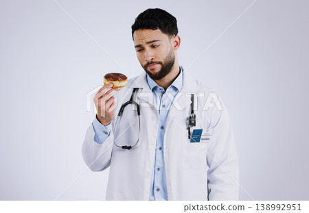 Doctor, diet and thinking with donut in hand for nutrition in studio, white background or mockup space. Nutritionist, choice and man with doubt or decision for health with dessert, sweets or candy 138992951
