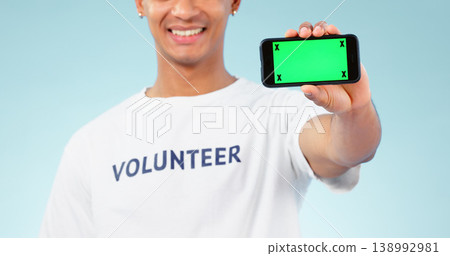 Hand, phone and green screen with a volunteer man in studio on blue background for marketing or charity. Smile, space or advertising and a person showing chromakey on a display with tracking markers 138992981