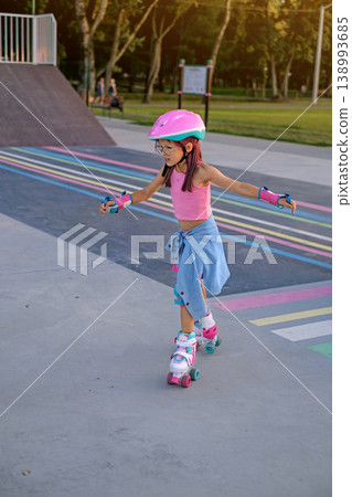 A child in a full protective sports uniform and helmet learns to keep his balance while roller skating. 138993685