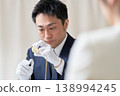 一位戴著白手套的男性鑑定師正在用放大鏡檢查一件物品。 138994245