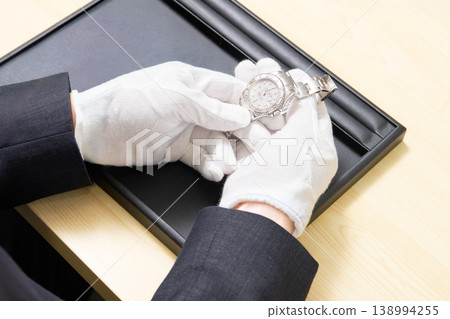 The appraiser, wearing white gloves, examines the condition of the watch during the appraisal. 138994255