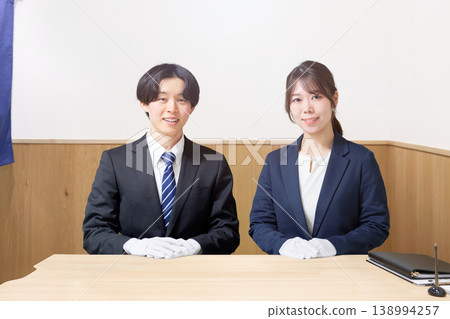 Male and female staff members, dressed in suits and wearing white gloves, sit at the customer service counter. 138994257