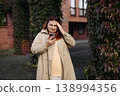 Young woman looking at smartphone with confused expression while standing outdoors near brick building and green ivy. 138994356