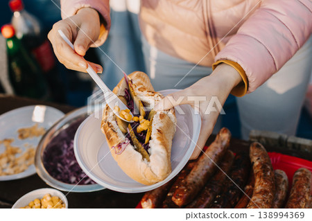 Woman cooking a delicious hotdog on a grill picnic outside. Woman cooking a delicious hotdog on a grill picnic outside. 138994369