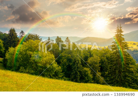 sunset over mountain hay field. alpine countryside summer landscape with green valley behind the woods on the grassy slope. cloudy sky. spectacular highland background under the rainbow 138994690