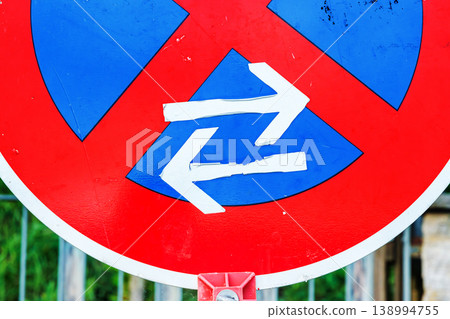 Close up detail of selfmade white directional arrows on a red and blue traffic sign surface. urban road regulation symbol with bold color contrast 138994755