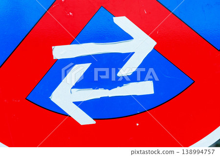 Close up detail of selfmade white directional arrows on a red and blue traffic sign surface. urban road regulation symbol with bold color contrast 138994757