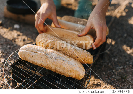 Woman cooking buns for hotdogs on a grill picnic outside. Woman cooking buns for hotdogs on a grill picnic outside. 138994776