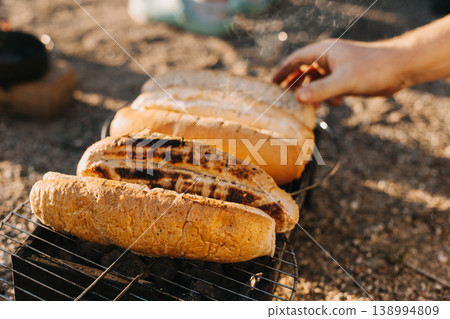 Woman cooking buns for hotdogs on a grill picnic outside. Woman cooking buns for hotdogs on a grill picnic outside. 138994809