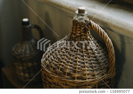 Vintage wicker wine bottles near the window. 138995077
