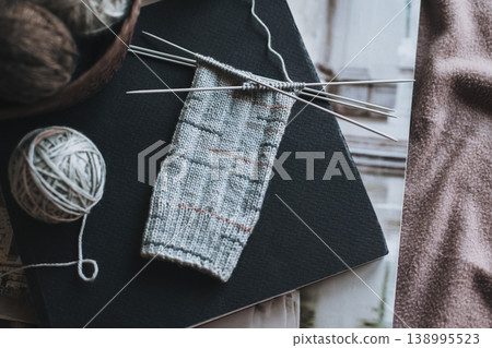 Hand knitted socks with needles and yarn ball in a basket. Concept for handmade and hygge slow life. Hand knitted socks with needles and yarn ball in a basket. Concept for handmade and hygge slow life. 138995523