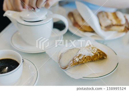 Sweet cannoli stuffed with cream and cup of black coffee for breakfast on a table in a cafe. 138995524