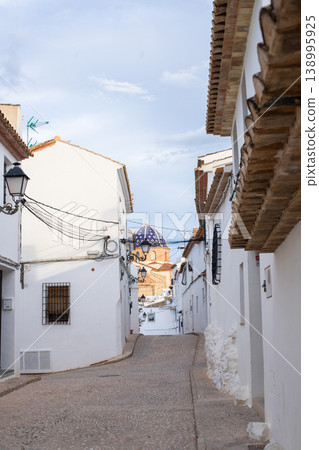 Charming cobblestone street winding through the traditional whitewashed buildings of Altea city, Spain, leading to the distinctive blue domed church, perfect for exploring on family holidays 138995925