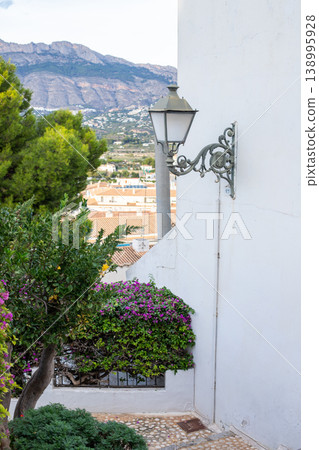 Charming Altea street scene with ornate lamp, vibrant bougainvillea, traditional houses, and scenic mountains under a clear Spanish sky during a family vacation 138995928