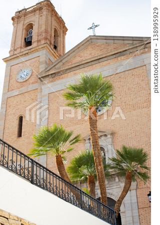 Historic Altea church bell tower and facade with lush palm trees under a bright sky, a beautiful Spanish travel destination for family holidays 138995929