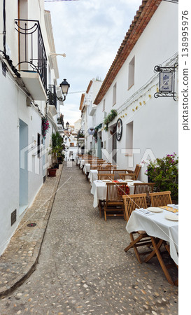 Altea Spain charming cobblestone street adorned with inviting outdoor restaurant tables, nestled between traditional whitewashed buildings for family holidays 138995976