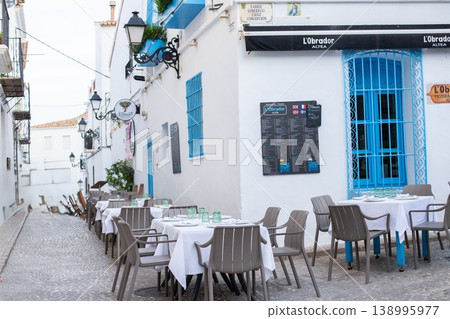 Strolling through a picturesque Altea street with outdoor restaurant tables set for lunch during a warm family holiday in Spain 138995977