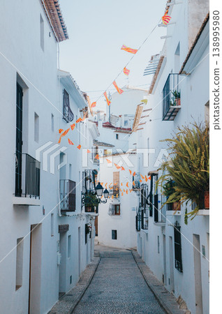 Picturesque narrow street in Altea Spain featuring traditional whitewashed houses balconies and festive bunting creating a welcoming atmosphere for family holidays and travel adventures 138995980