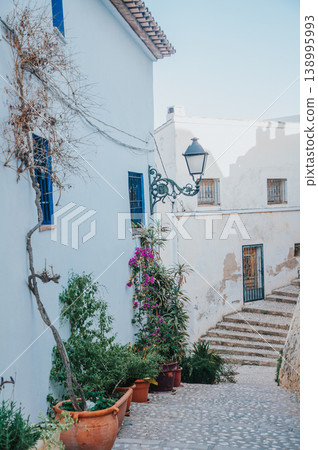 Altea Spain charming street scene with traditional white architecture, blue windows, vibrant plants, and ancient cobblestones, perfect for serene Mediterranean travel and family holidays 138995993