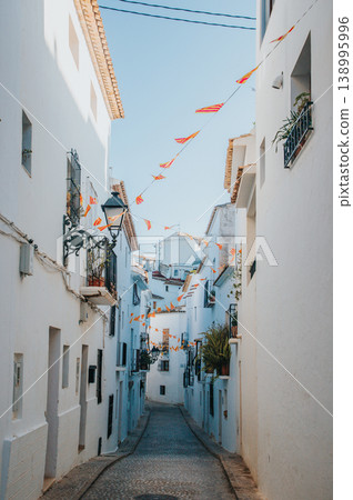 Whitewashed Altea street on a sunny day with festive bunting, inviting visitors to explore the charming old town during their Spanish family holiday 138995996
