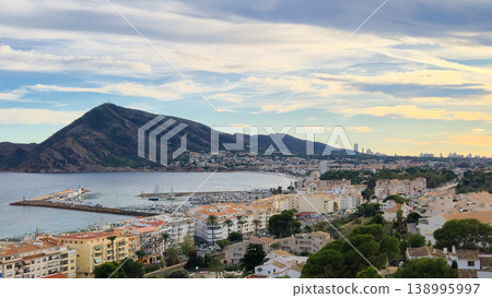 Panoramic view of Altea city in Spain showcasing the beautiful coastline, bustling harbor with boats, and majestic mountains under a dynamic cloudy sky 138995997