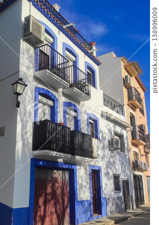 Traditional white and blue buildings with classic wrought iron balconies lining a sunny street in Altea, Spain, showcasing the city's unique architectural charm for memorable family holidays 138996009