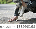 A man walks his dog, a Chihuahua, and checks the ground temperature with his hand. 138996168