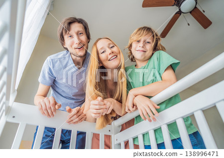 Parents and older brother looking into baby crib from infant point of view. Family smiling down at newborn with love and care. Sibling bonding, parenthood, childhood memory and connection concept Parents and older brother looking into baby crib from infant point of view. Family smiling down at newborn with love and care. Sibling bonding, parenthood, childhood memory and connection concept 138996471