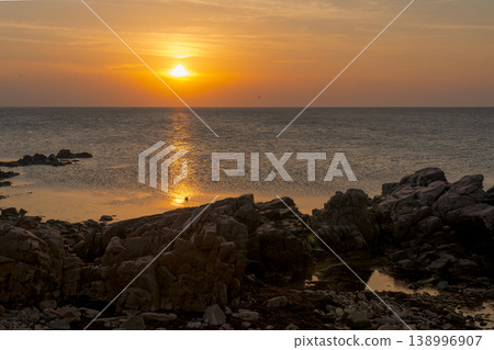 The golden sunset sinking behind the rocky coastline and the path of light reflecting on the surface of the sea. 138996907