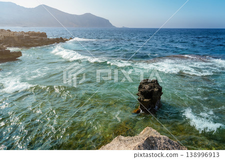 Crystal-clear waters with mountains in the background and white waves crashing against the rocky shore. Crystal-clear waters with mountains in the background and white waves crashing against the rocky shore. 138996913