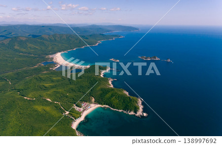 Aerial panorama of a beautiful coastline featuring a long white sand beach, lush green mountains, and calm blue sea. Aerial panorama of a beautiful coastline featuring a long white sand beach, lush green mountains, and calm blue sea. 138997692