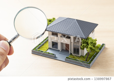 Hands observing a house model with a magnifying glass 138997867