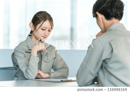 Male and female manufacturing and factory workers in work clothes holding a meeting/discussion in a conference room. Male and female manufacturing and factory workers in work clothes holding a meeting/discussion in a conference room. 138998169