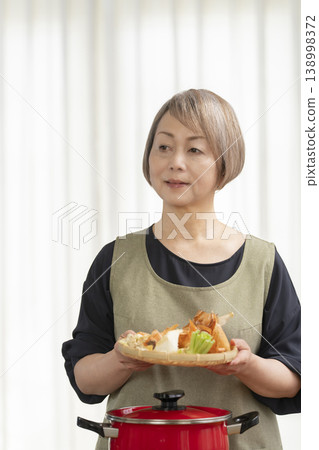 廚房裡,一位老婦人正在煮蔬菜湯。 廚房裡,一位老婦人正在煮蔬菜湯。 138998372