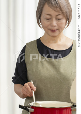 廚房裡,一位老婦人正在煮蔬菜湯。 廚房裡,一位老婦人正在煮蔬菜湯。 138998373