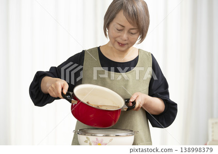 廚房裡,一位老婦人正在煮蔬菜湯。 廚房裡,一位老婦人正在煮蔬菜湯。 138998379