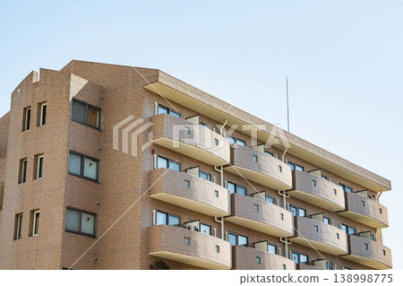 The exterior of a brown tiled apartment building against a blue sky. The exterior of a brown tiled apartment building against a blue sky. 138998775