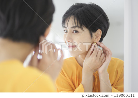 一位女士對著鏡子戴耳環。晨間日常。自然生活。 139000111